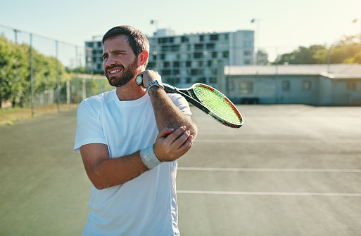 Shot of a sporty young man holding his elbow in pain while playing tennis on a tennis court