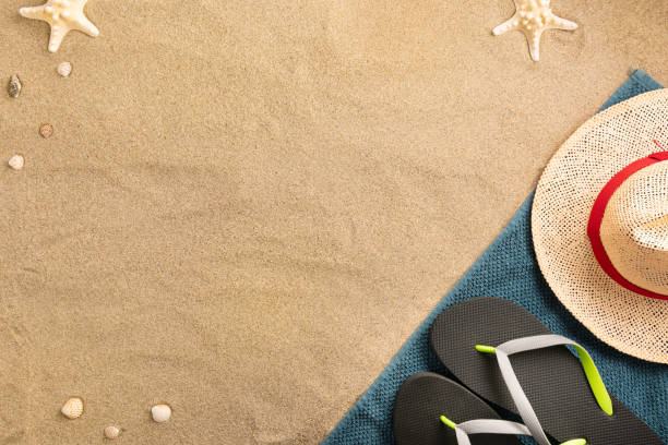 istock Beautiful summer holiday beach background with straw hat and flip flops on sand background, border design, top view with copy space 1217815950