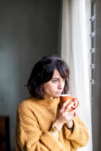istock Concerned woman staring out the window holding hot drink 1217819202