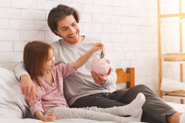 Girl putting money in piggy bank, spending time with dad Father teaching little daughter to save money in piggy bank, financial literacy, home interior, copy space financial literacy stock pictures, royalty-free photos & images