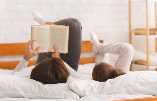 istock Father and little daughter lying on bed, reading book 1217820129