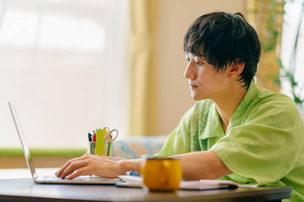 Man comfortably using laptop at home A young man is comfortably using a laptop at home. only japanese stock pictures, royalty-free photos & images