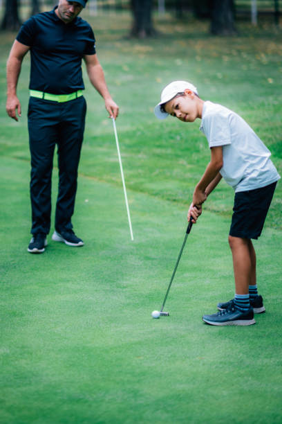 ゴルフパッティングトレーニング。パッティンググリーンで練習する若い男の子とゴルフインストラクター - golf green practicing sports training ストックフォトと画像