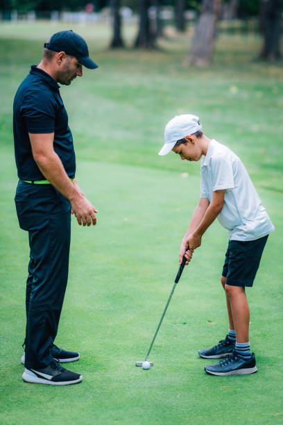 ゴルフパッティングトレーニング。パッティンググリーンで練習する若い男の子とゴルフインストラクター - golf green practicing sports training ストックフォトと画像