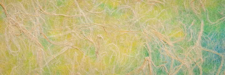 Natural Thai mulberry kozo paper against green, blue and yellow marbled paper, panorama banner