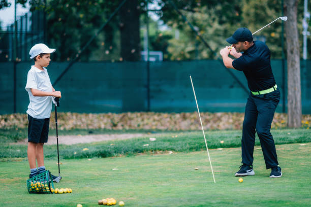 golfe – treinamento pessoal. instrutor de golfe ensinando o garoto a jogar golfe. - golf green practicing sports training - fotografias e filmes do acervo