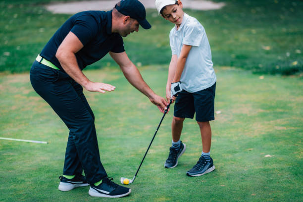 golfe – treinamento pessoal. instrutor de golfe ensinando o garoto a jogar golfe. - golf green practicing sports training - fotografias e filmes do acervo