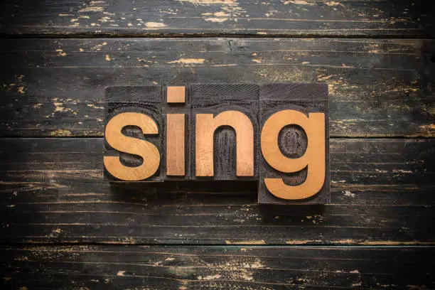 The word "SING" written in vintage wood letterpress type on a vintage rustic background.