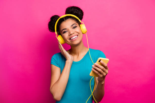 Photo of pretty funny dark skin lady hold telephone hands listen fm music modern technology earphones good mood wear blue casual t-shirt isolated magenta color background Photo of pretty funny dark skin lady hold telephone hands listen fm music, modern technology earphones good mood wear blue casual t-shirt isolated magenta color background topknot stock pictures, royalty-free photos & images