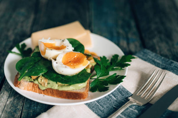 istock Toast with avocado, boiled egg spinach and parsley on white plate with knife and fork on serviette and rustic blue wooden background 1217837978