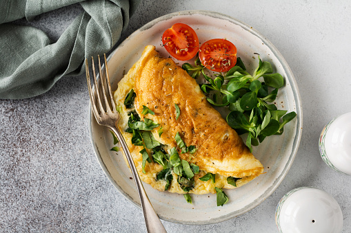 Stuffed omelette with tomatoes, red bell pepper, cream cheese and corn or lamb's lettuce on light concrete background with copy space. Healthy diet food for breakfast. Top view, flat lay.