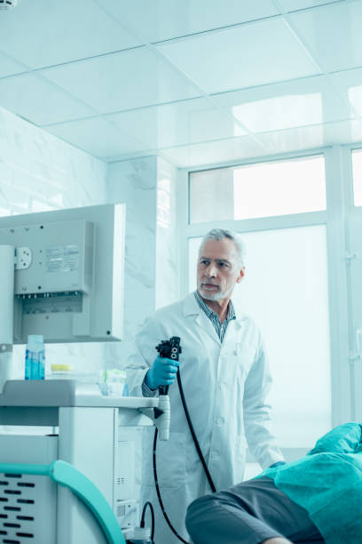 Concentrated doctor ready to conduct endoscopy stock photo Professional doctor looking at the screen while standing with an endoscope near his patient gastroenterology photos stock pictures, royalty-free photos & images
