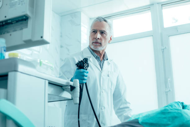 Serious doctor performing endoscopy in his clinic Calm mature medical worker standing with an endoscope and looking at the screen stock photo gastroenterology photos stock pictures, royalty-free photos & images