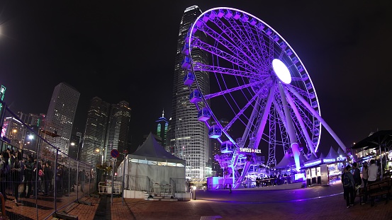 Hong Kong, China - December 5, 2016: popular Ferris Wheel in Hong Kong island at sunset near Central Waterfront Promenade with landmark buildings in background at night.