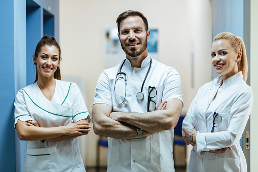 Team of confident doctors standing with arms crossed at medical clinic and looking at camera.