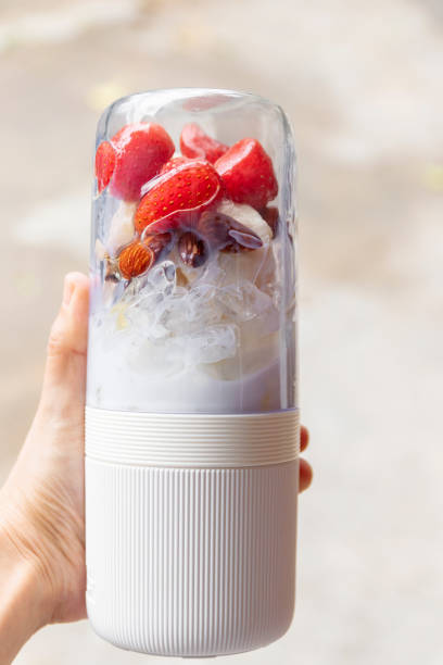 woman hand holding portable blender with healthy fruits; getting ready for making a smoothie. fresh strawberry, banana, almond, honey and milk with ice; healthy and fresh concept. - vitality food food and drink berry fruit imagens e fotografias de stock