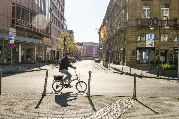 Coronavirus lockdown. Frankfurt, Germany. April 5, 2020. Old man riding bicycle on empty street wearing a mask. Profile view.