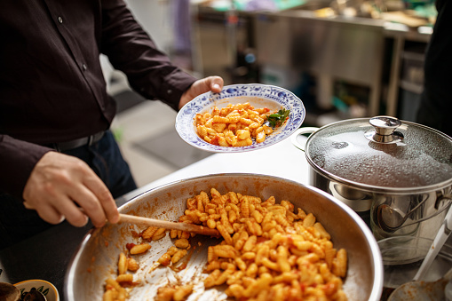 Man filling his plate with pasta at a restaurant. Close-up of a man serving himself pasta at buffet lunch.