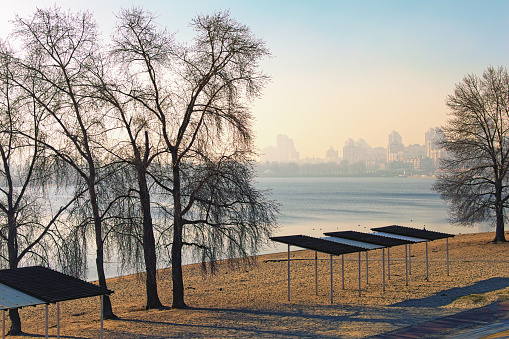 Scenic landscape view of Dnieper River and empty beach in modern Obolon district. Embankment with skyscrapers in morning smog in the background. Kyiv, Ukraine