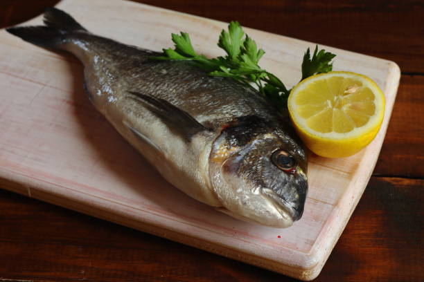 istock Flat composition with fresh bream fish, lemon and parsley on wooden board 1217849736