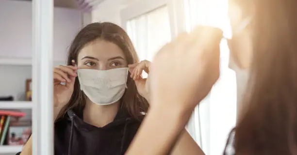 Photo of young girl wearing medical protective face mask looking mirror stay at home