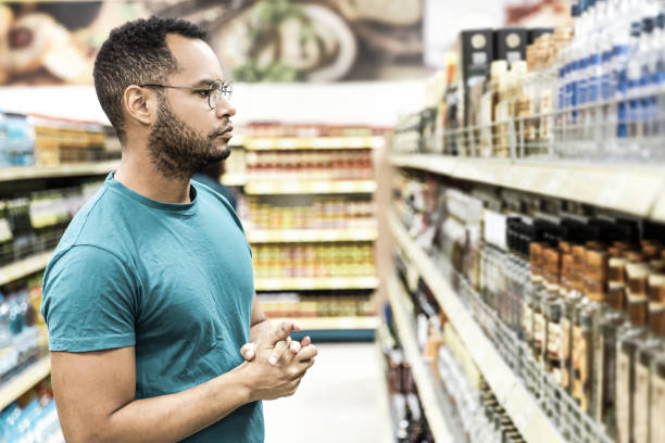 Focused African American man choosing alcohol drinks Focused African American man choosing alcohol drinks. Serious bearded guy standing in aisle and looking at drinks. Shopping concept alcohol shop stock pictures, royalty-free photos & images