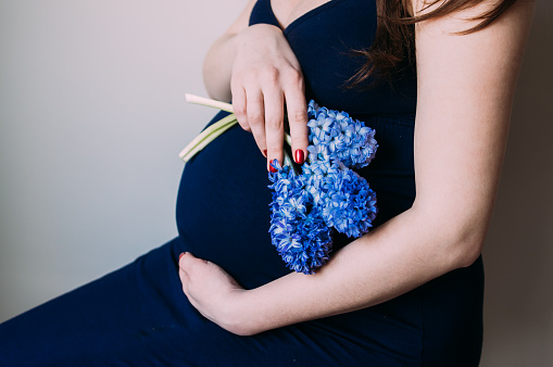 Pregnant woman in dark blue dress sitting with bouquet of flowers