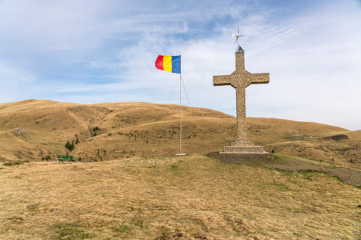 Landscape in the Bucegi Natural Park. Yellow shiny vegetation, the Romanian flag waving in the wind, a stone cross