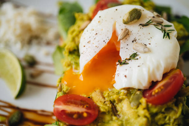 sandwich with smashed avocado and poached egg with tomatoes on the white plate on a white table - poached egg imagens e fotografias de stock