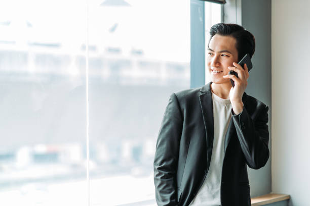 istock Asian chinese smiling young businessman looking away while using mobile phone at his office 1217851858