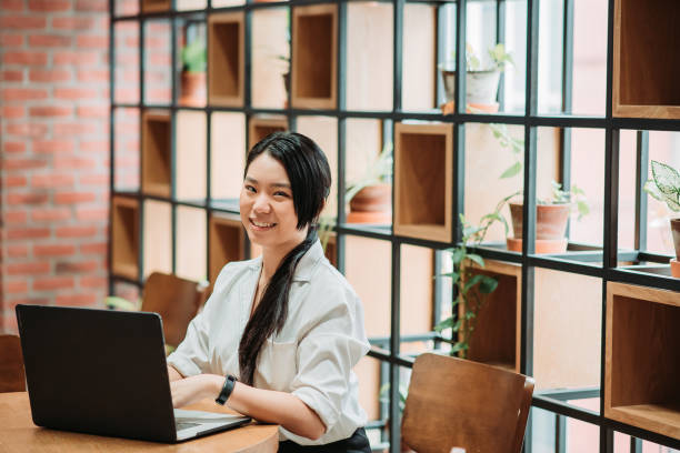 istock Asian chinese female smiling young executive using laptop and looking at camera in office co-sharing work place 1217854067