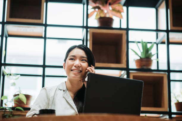istock Asian chinese female smiling young executive using mobile phone talking with client in office co-sharing work place 1217854110
