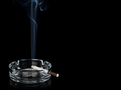 Smoke from cigarette with the dark filter in glass ashtray it is isolated on the black