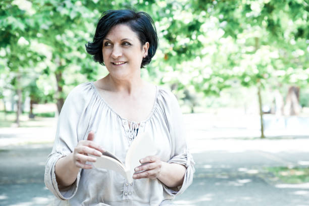 istock Smiling woman holding book in park 1217857718