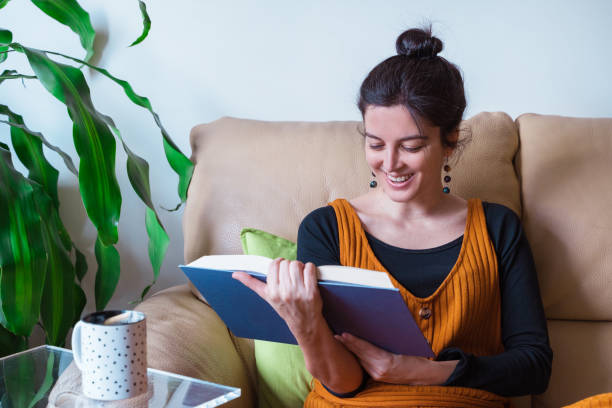 istock Horizontal side view of woman sit on the couch reading a book. 1217859762