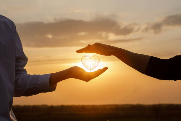 The concept of a love relationship between people. The concept of a love relationship between people. Hands interacts with a heart on a background of sunny sunset. commits stock pictures, royalty-free photos & images