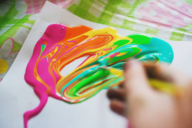 A boy experiments with a paintbrush & colourful acrylic paints.
