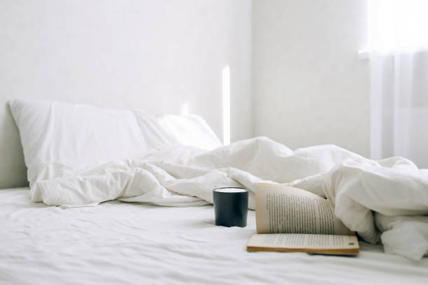 istock Coffee or tea cup and an open book on the bed. 1217867474