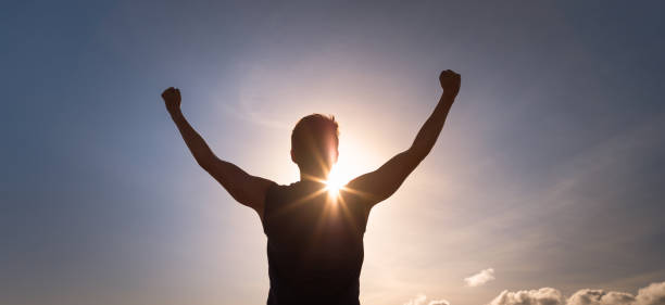 Strong young man with fist up to the sunset sky flexing his arms with bright rays of sunshine. People strength, power and determination concept. record breaking stock pictures, royalty-free photos & images