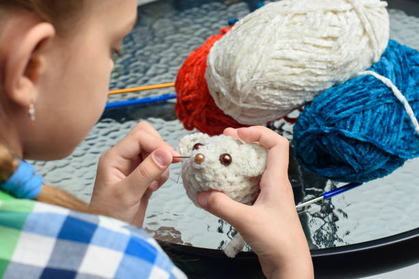 Girl sews on the eyes of a homemade soft toy mouse stock photo