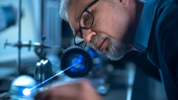 高精度レーザー機器を使用したメガネの中年エンジニアのクローズアップ肖像画、レンズを使用し、精度が必要なエレクトロニクスのための光学をテスト - accuracy ストックフォトと画像
