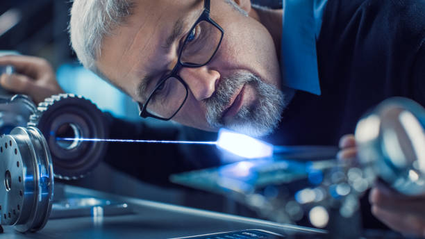 istock Close-up Portrait of Focused Middle Aged Engineer in Glasses Working with High Precision Laser Equipment, Using Lenses and Optics for Accuracy Electronics. Testing Superconductor Material 1217883721