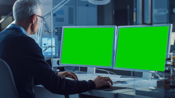 istock Professional Engineer Works on Computer with Two Green Mock-up Screen Displays. In the Background Industrial Electronics Design Agency. Over the Shoulder Shot 1217883745