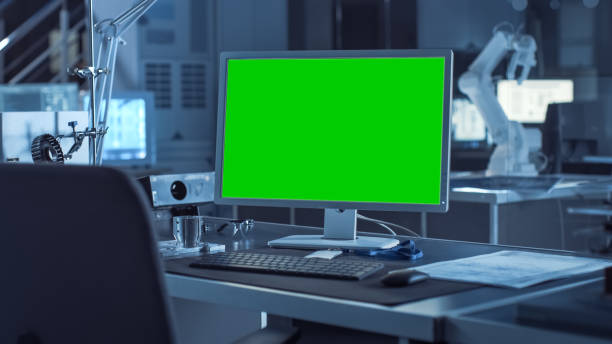 istock On the Desk Computer with Isolated Green Mock-up Screen Display. In the Background Robot Arm Concept Standing in Heavy the Dark.Industry Engineering Facility 1217883765