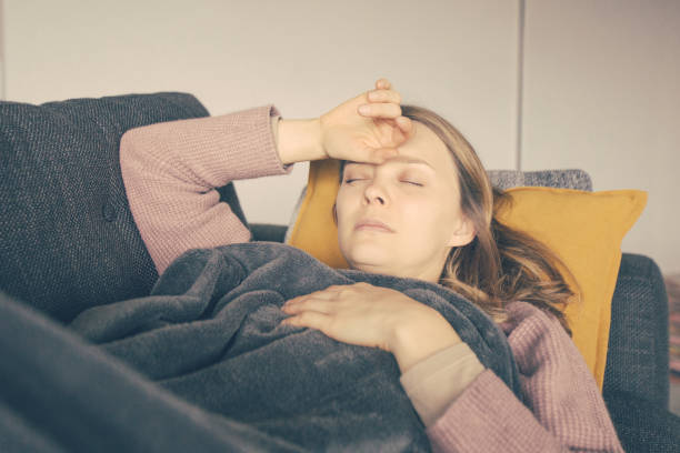 istock Sick woman lying on grey sofa at home, holding hands on chest 1217884463
