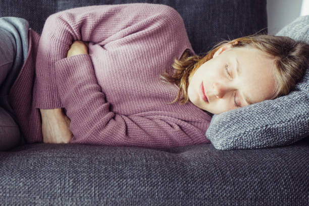 istock Sick woman lying on grey sofa at home, having legs bent 1217885988