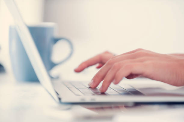 Close up of a womans hands typing on a laptop computer.