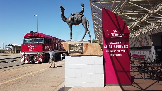 Alice Springs, Northern Territory, Australia - Aug 29, 2019: carriages of famous Ghan railway at a morning stop in Alice Springs Train Station and The Ghan Memorial: statue of Afghan worker and camel.