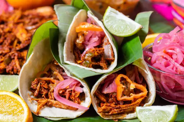 Tacos of cochinita pibil, traditional Mexican pit-roasted pulled pork dish from Yucatan, served with traditional condiments