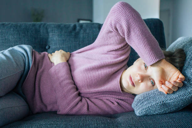 Sick woman lying on sofa, holding hands on stomach and head